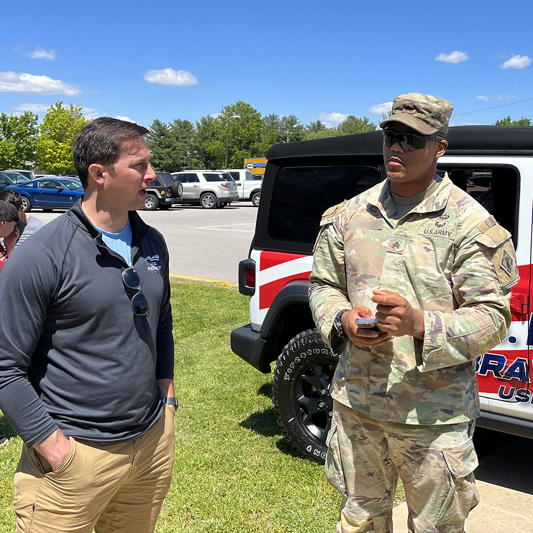 U.S. Patriot team member talks with a US Military soldier standing next to the tour Jeep