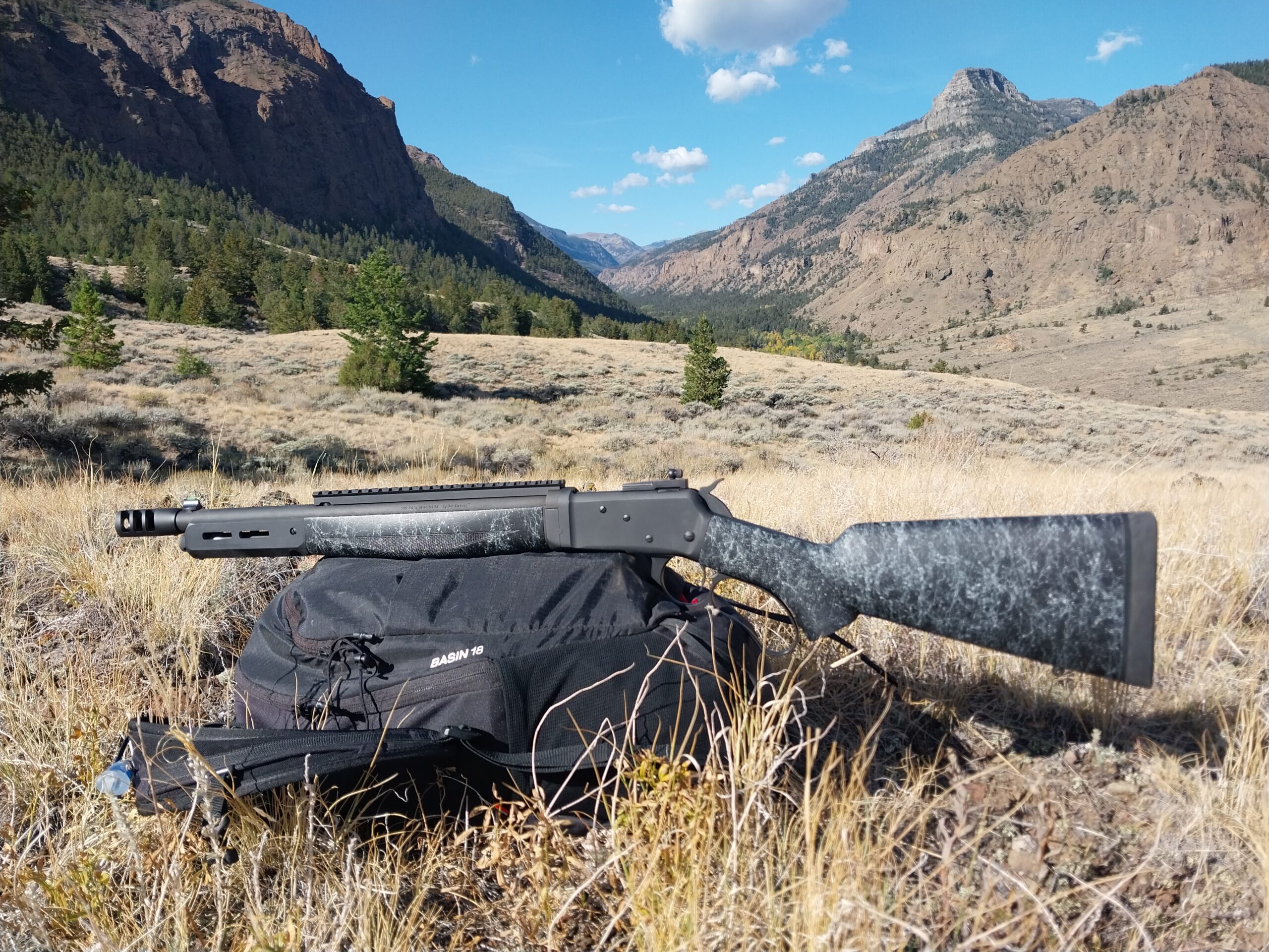 Tactical Take Down Lever Action resting on a backpack with mountains behind it